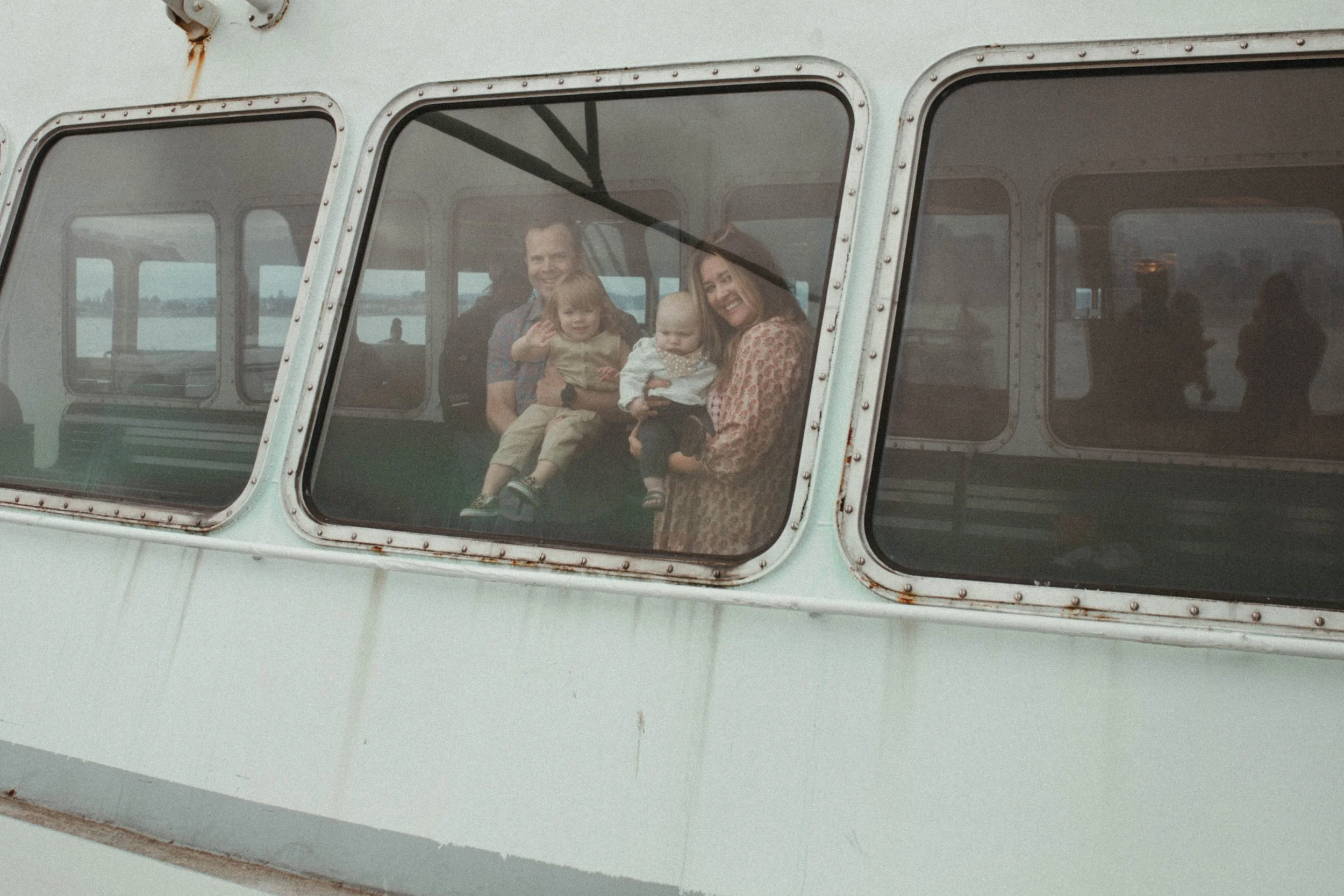 A family of four looking out the window of an old helicopter, smiling and waving.
