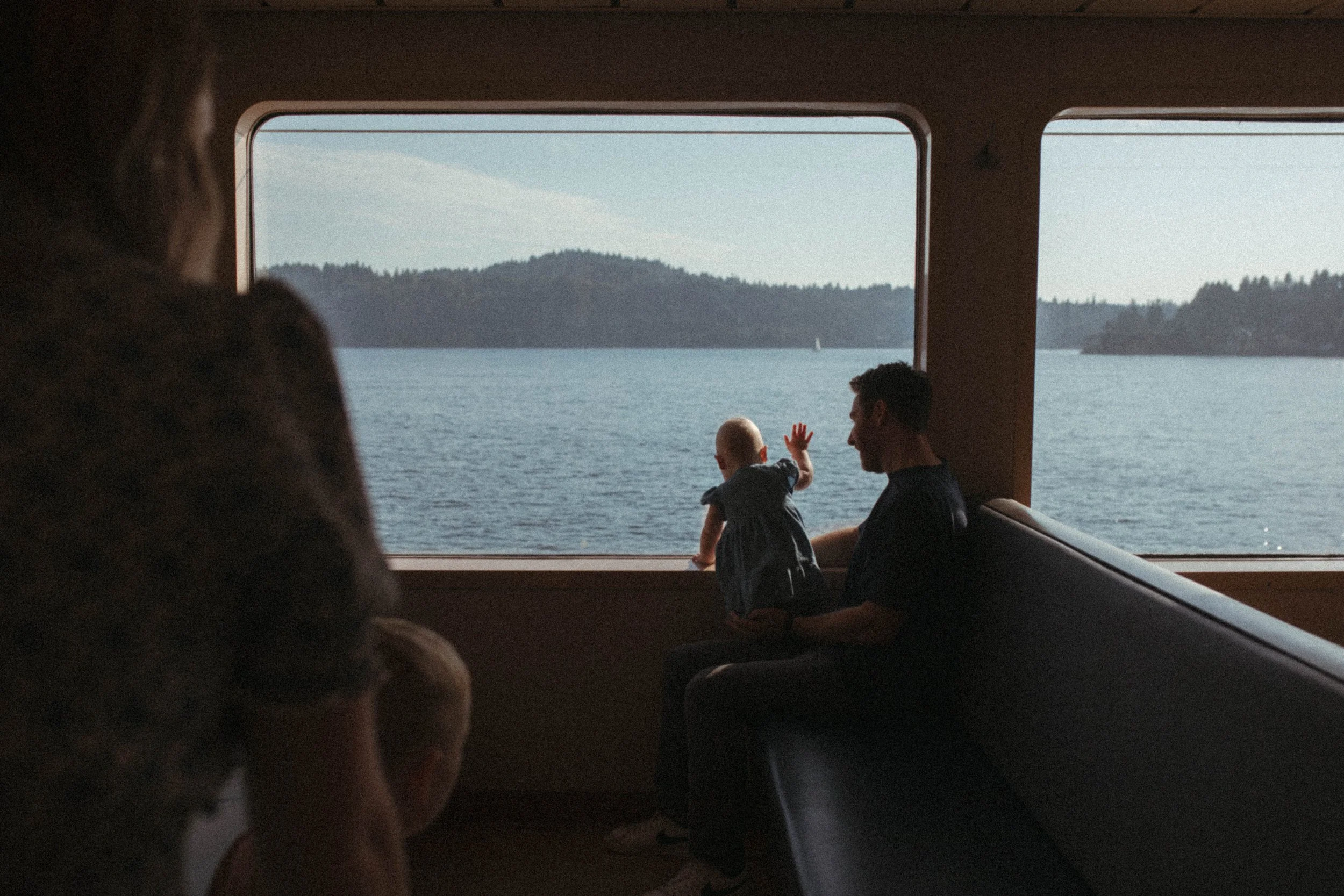 A man holding a child looking out a window at a body of water and mountains in the distance.