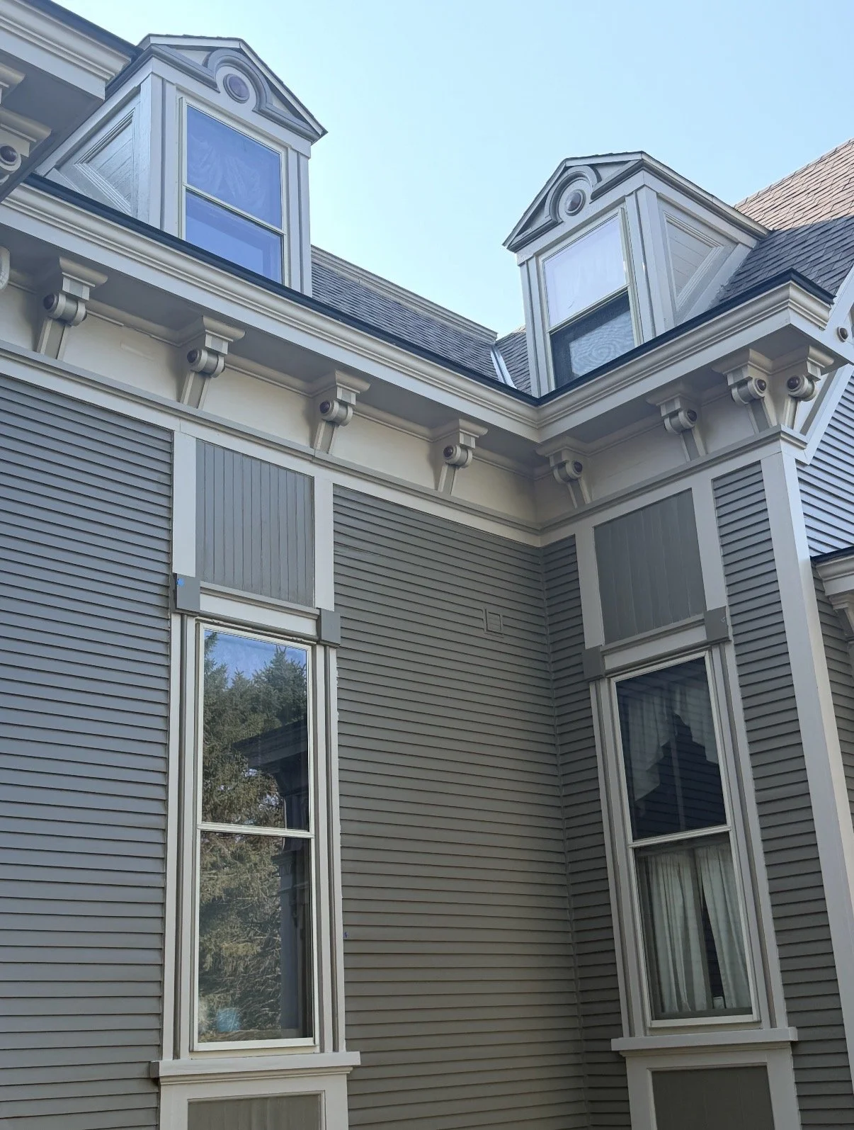 Close-up of an ornate Victorian-style gray house facade with decorative dormer windows, clapboard siding, and tall bay windows