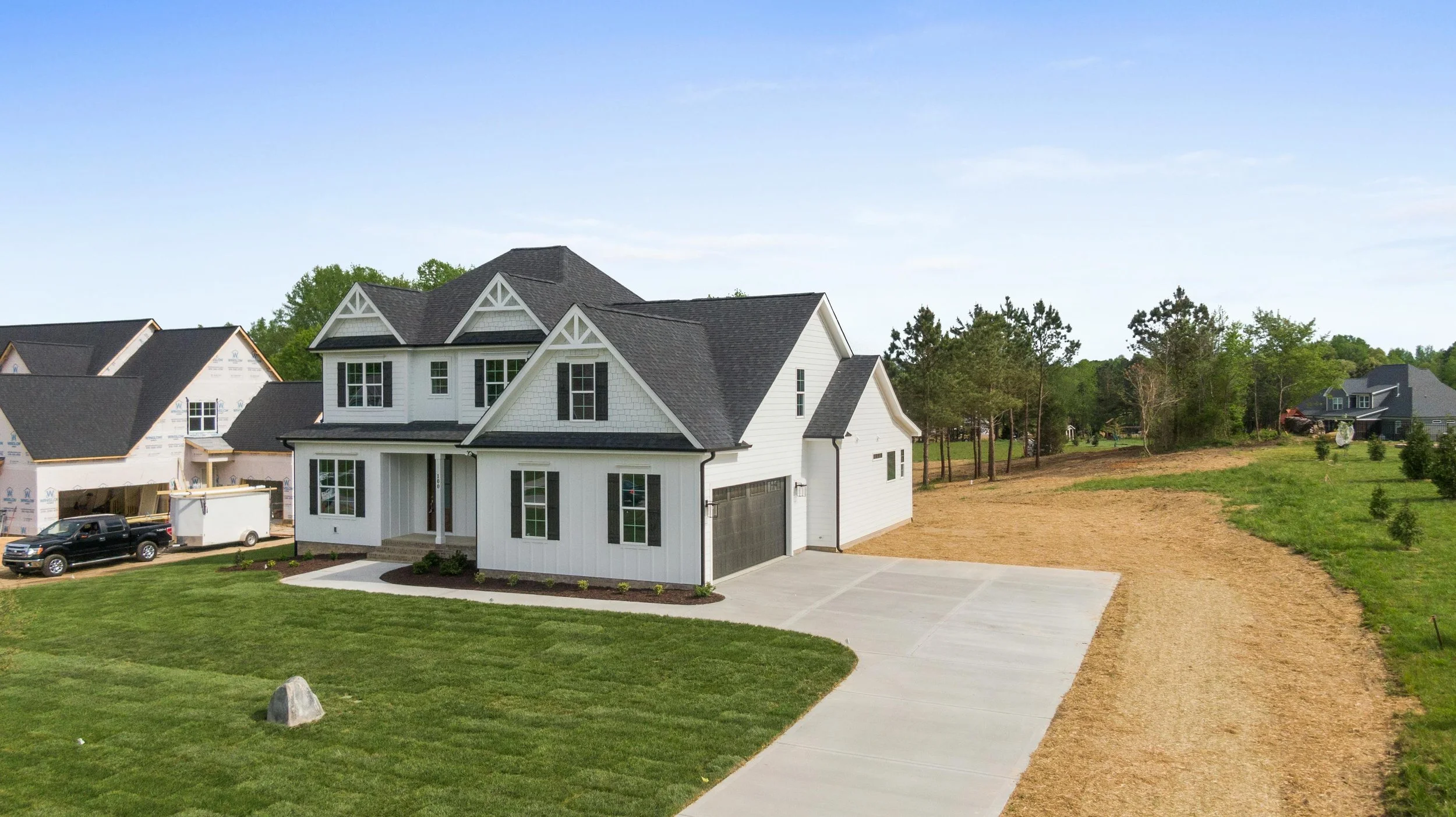Newly built two-story white house with black roof, front yard, and driveway on a suburban street under a clear blue sky.