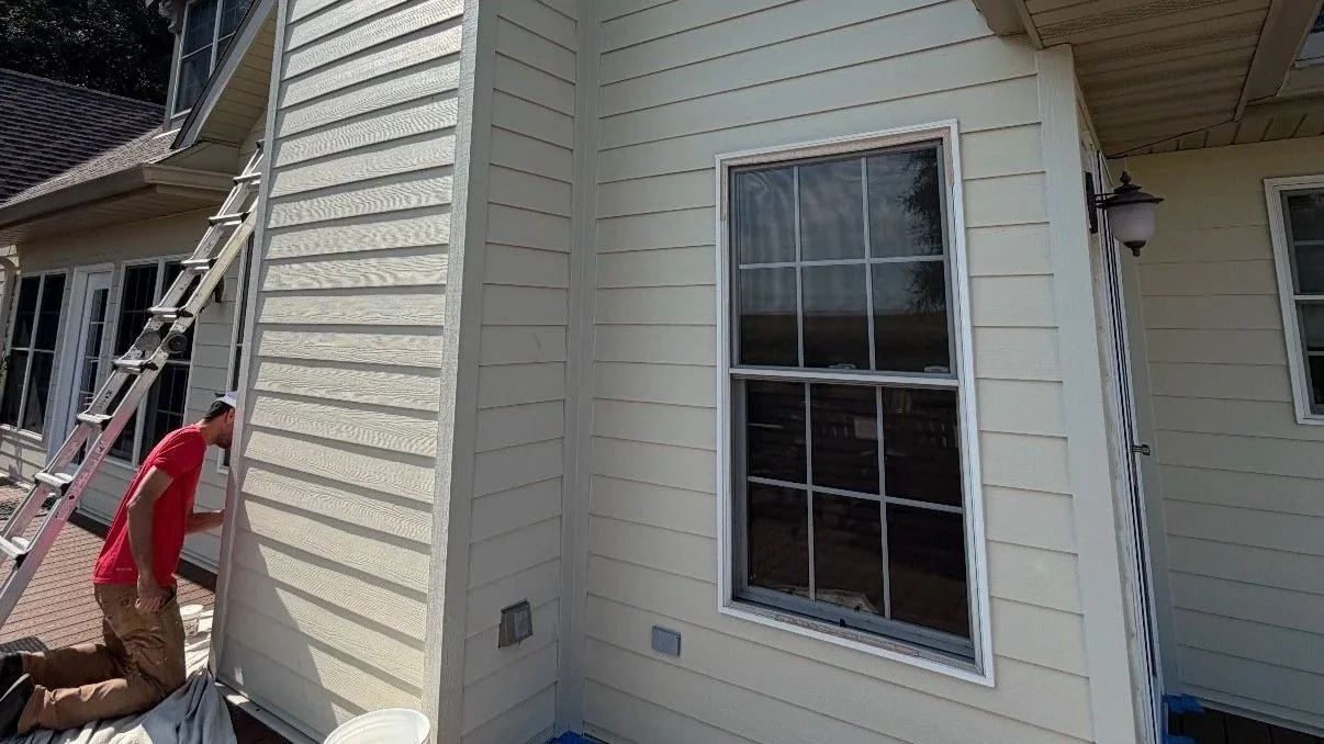 Worker kneeling beside a house exterior with a ladder and white siding
