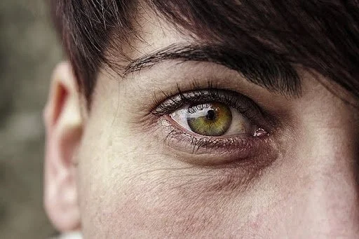 Close-up of a person's eye with green iris and dark hair.