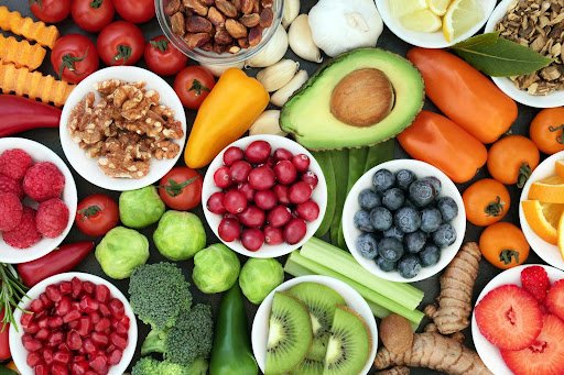 Assortment of fresh fruits and vegetables, including strawberries, cherry tomatoes, raspberries, green apples, avocados, blueberries, kiwifruit, broccoli, carrots, and lemon slices.