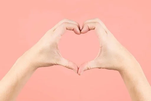 Hands forming a heart shape against a pink background.