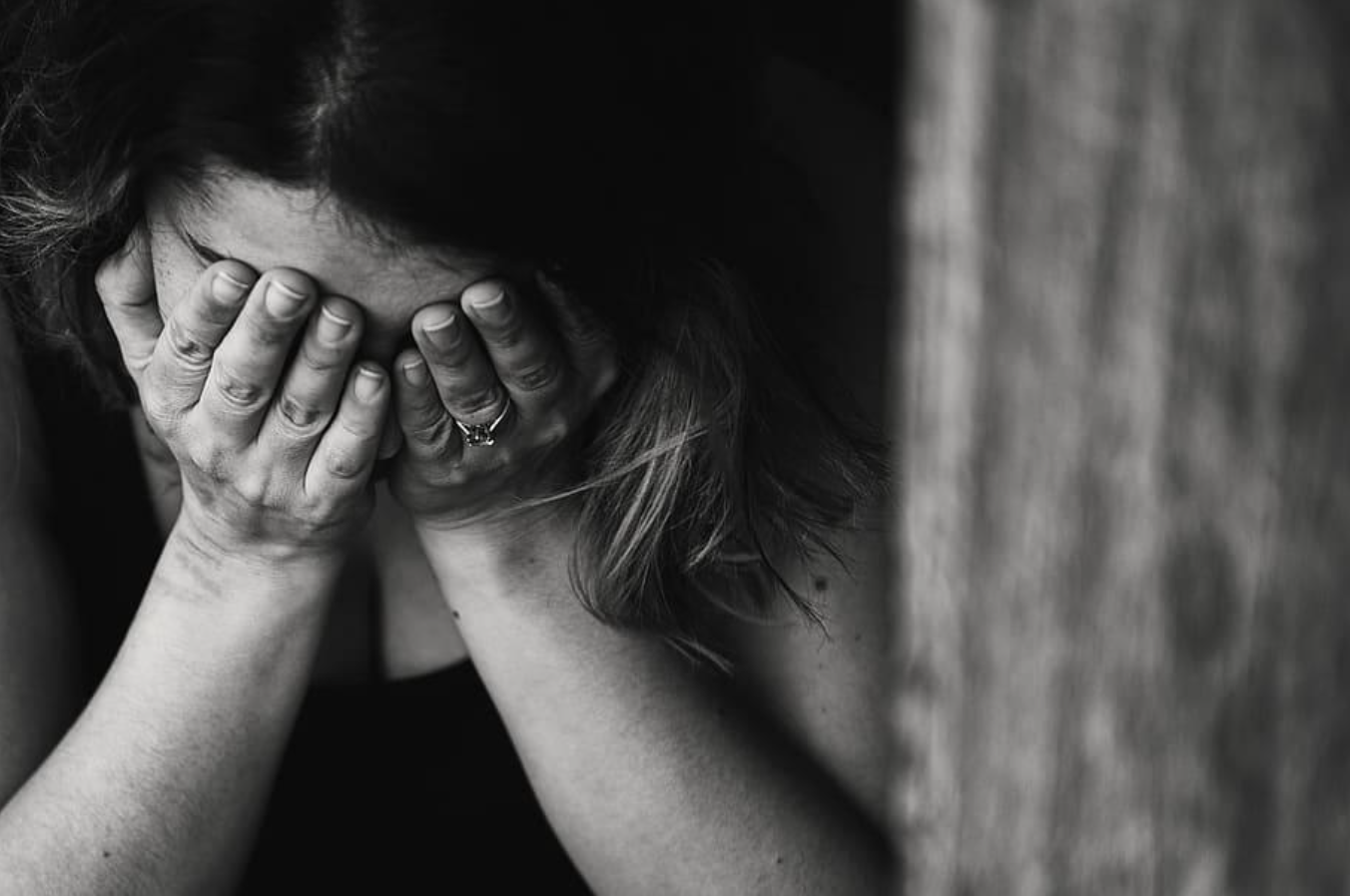 A woman with medium-length hair covering her face with her hands, resting her forehead on her hands, conveying distress or sadness.
