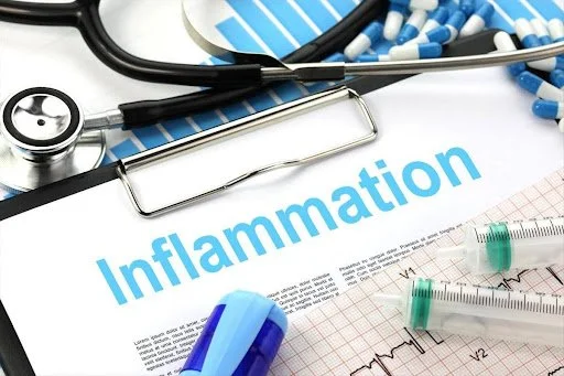 Medical clipboard with a stethoscope, pills, and syringes placed on a paper titled 'Inflammation' with a healthcare graph underneath.