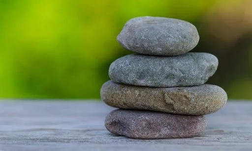 Stack of five smooth stones on a wooden surface with blurred green background.
