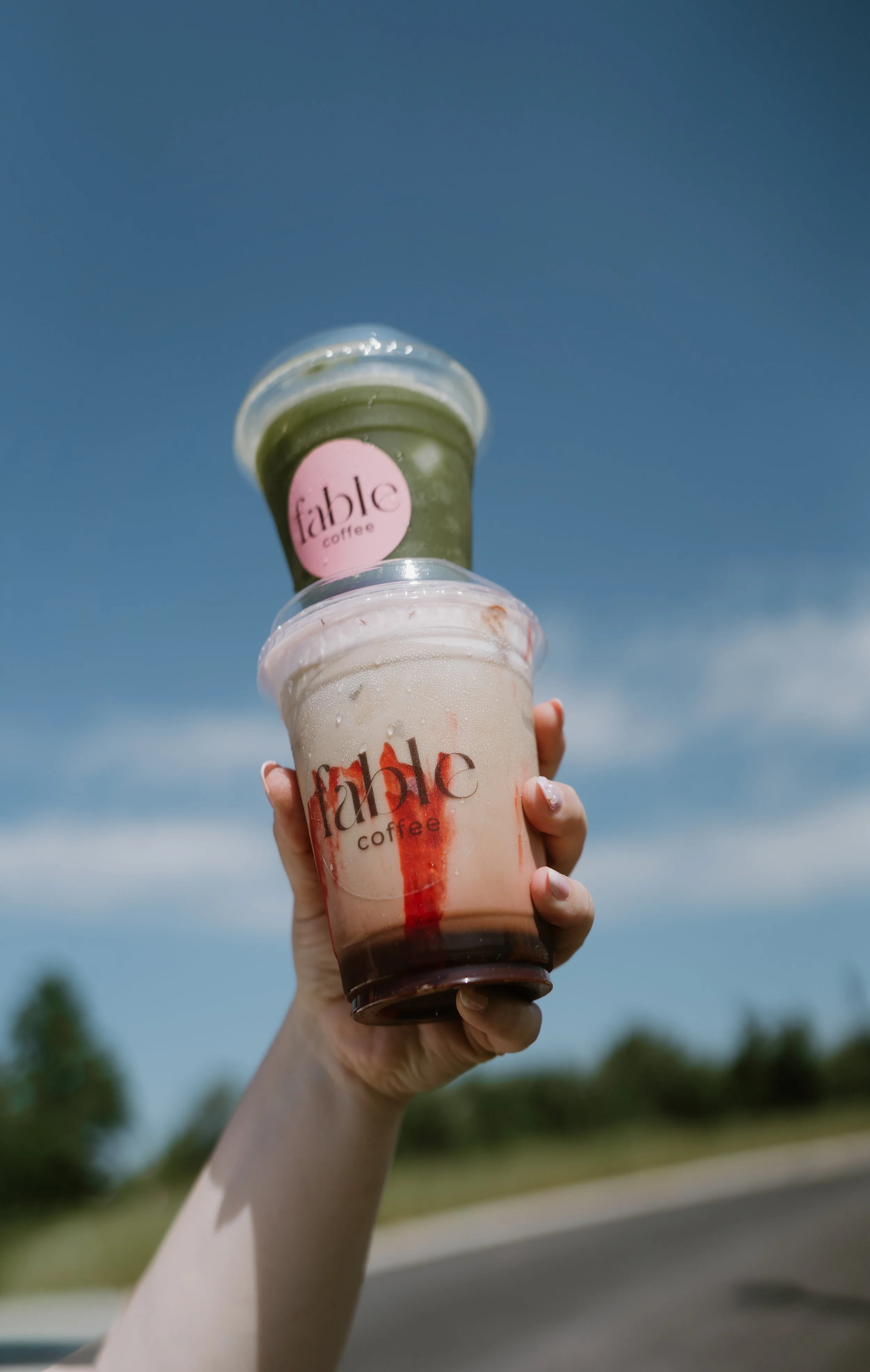 coffee and matcha being held against a blue sky
