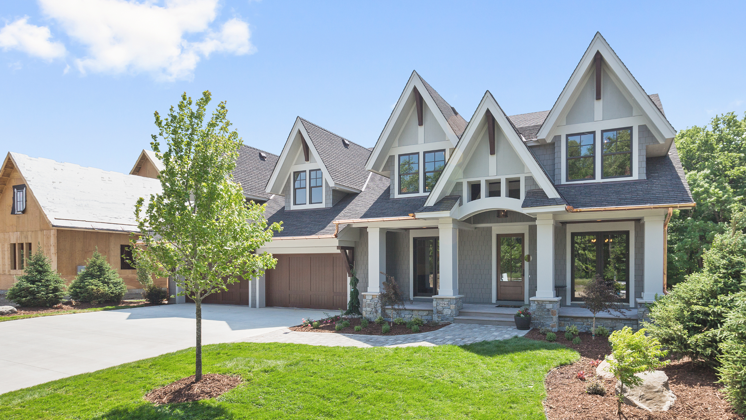 A newly built modern house with a large driveway, green lawn, and landscaped garden in a suburban neighborhood under a clear blue sky.