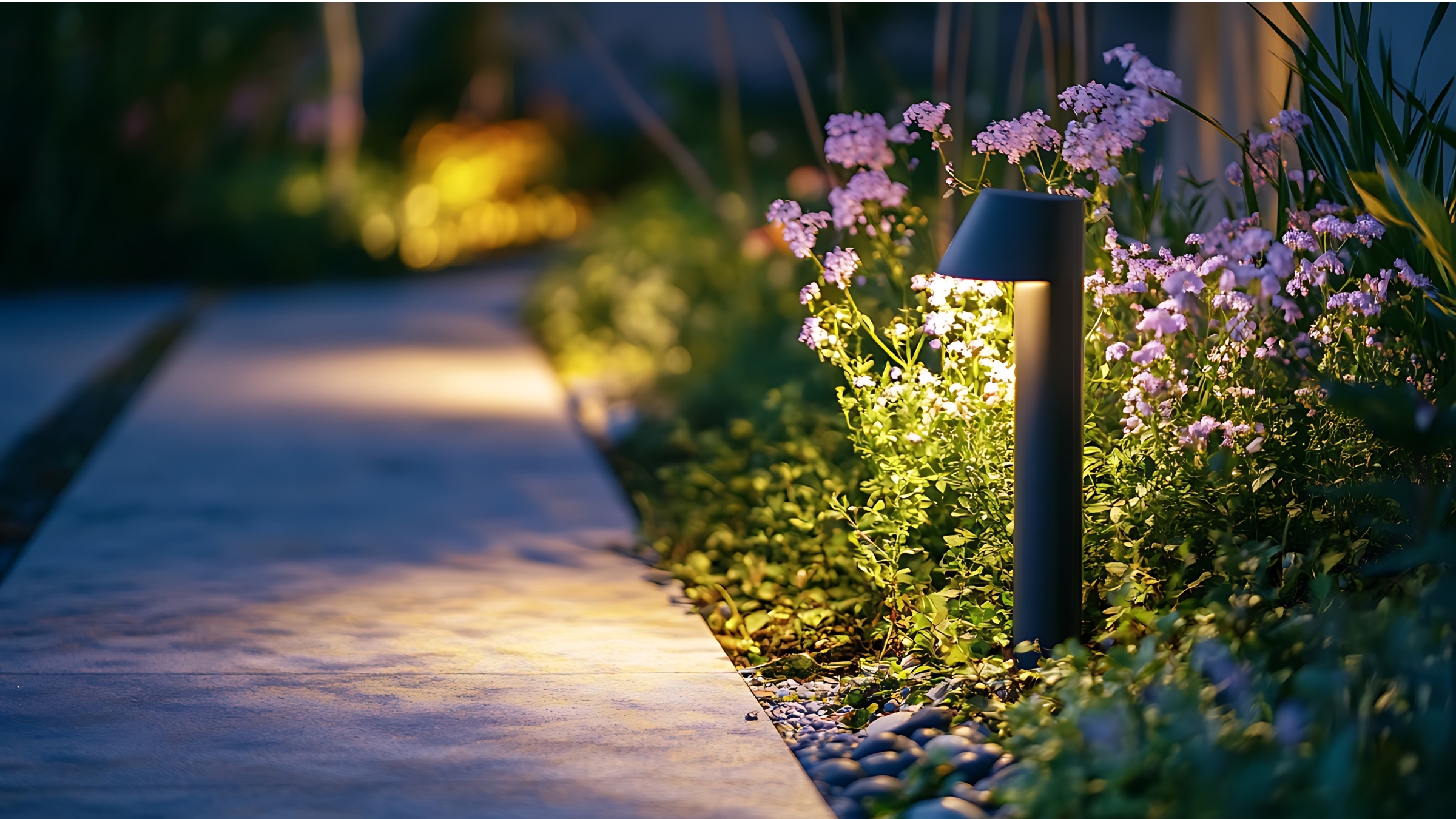 Outdoor garden pathway illuminated by a small LED spotlight among pink flowers and green plants at night.