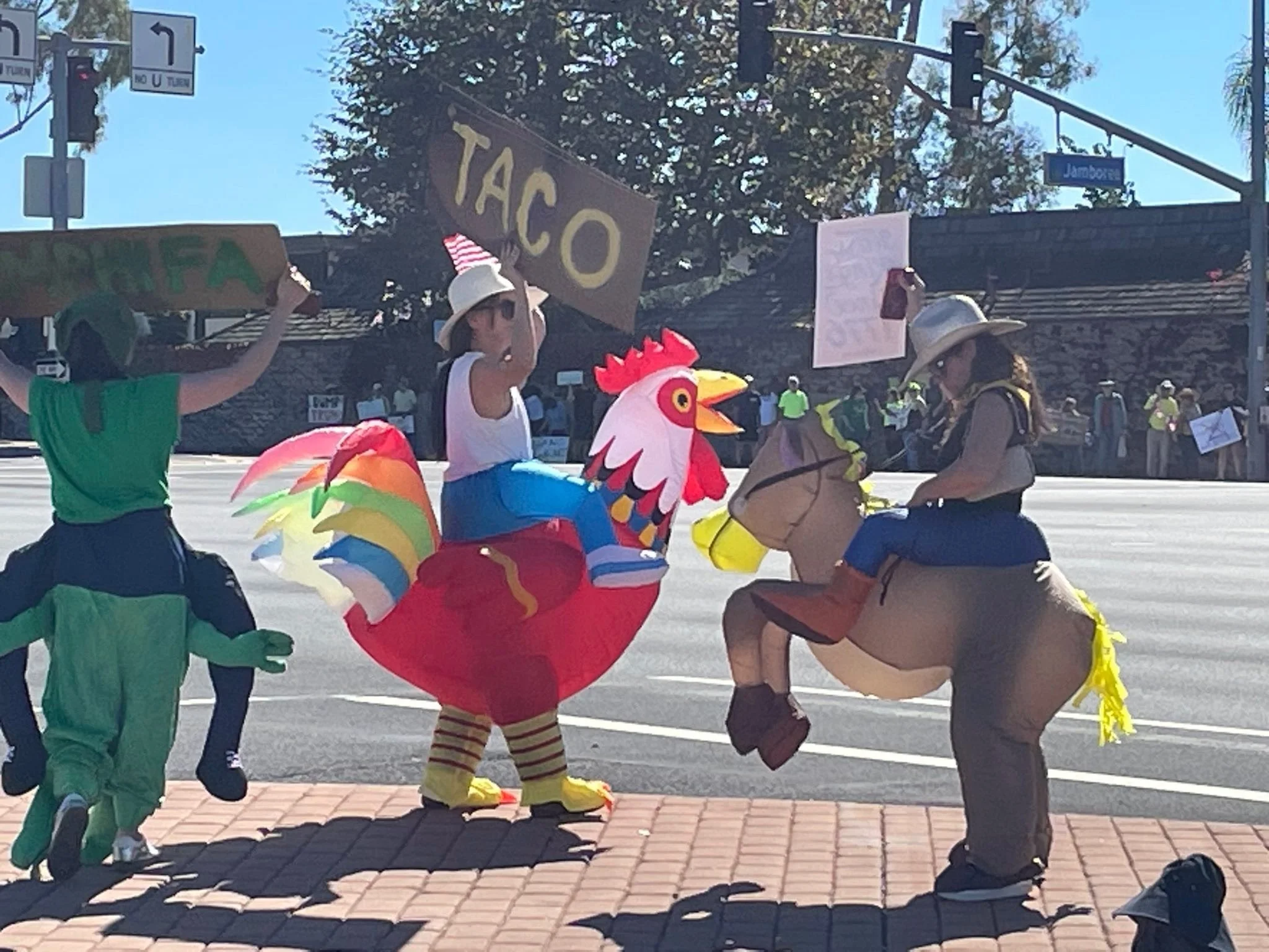 People dressed as farm animals, including a chicken, a cow, and a frog, participating in a parade or event on a city sidewalk.