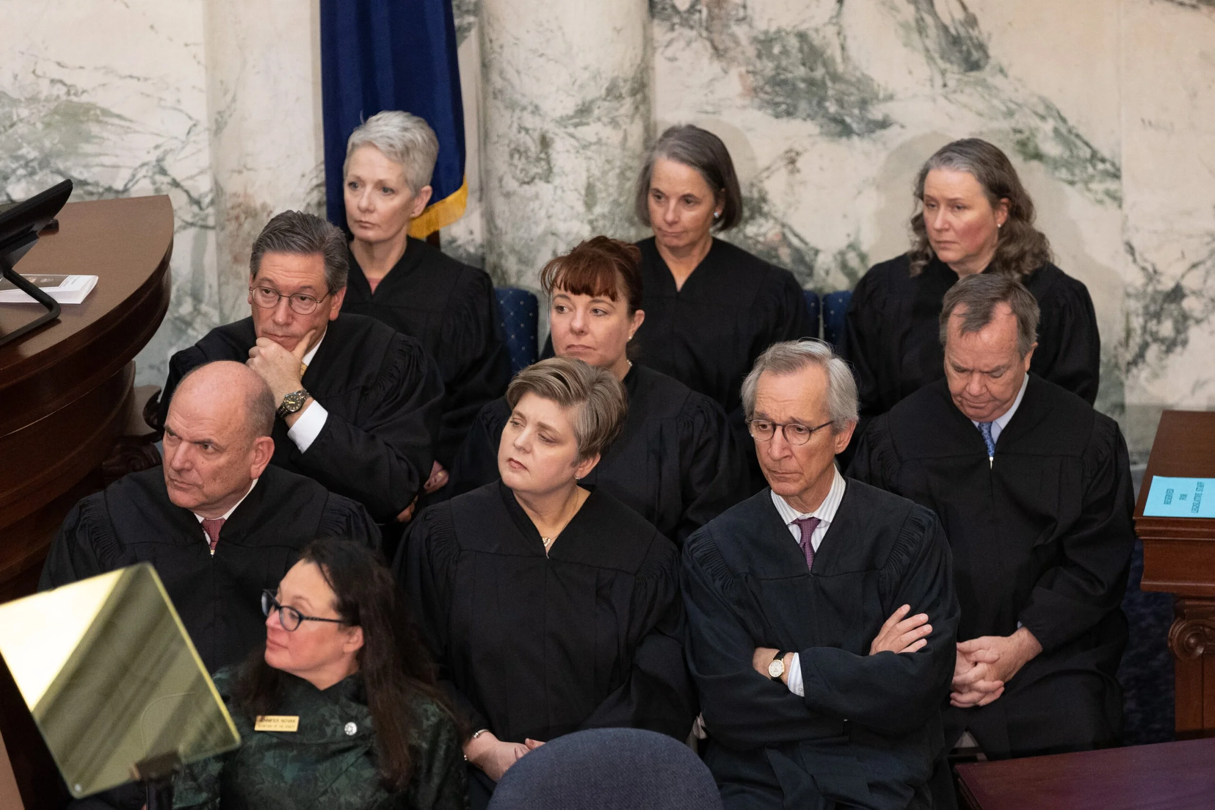Judges dressed in black robes seated in courtroom, some with hands clasped or resting on chins, engaging in legal proceedings.