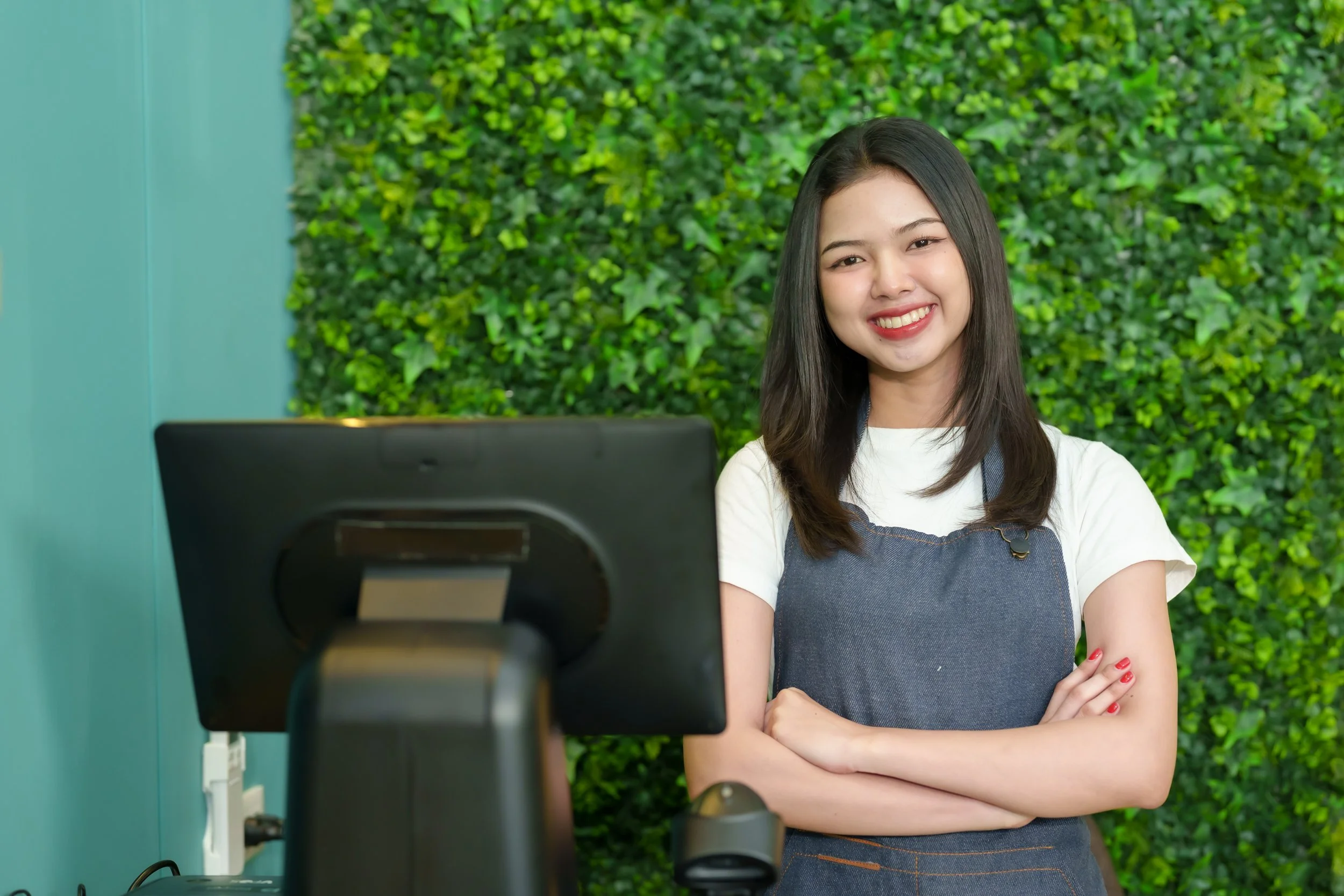 Retail staff member at checkout using POS system in store with green feature wall backdrop
