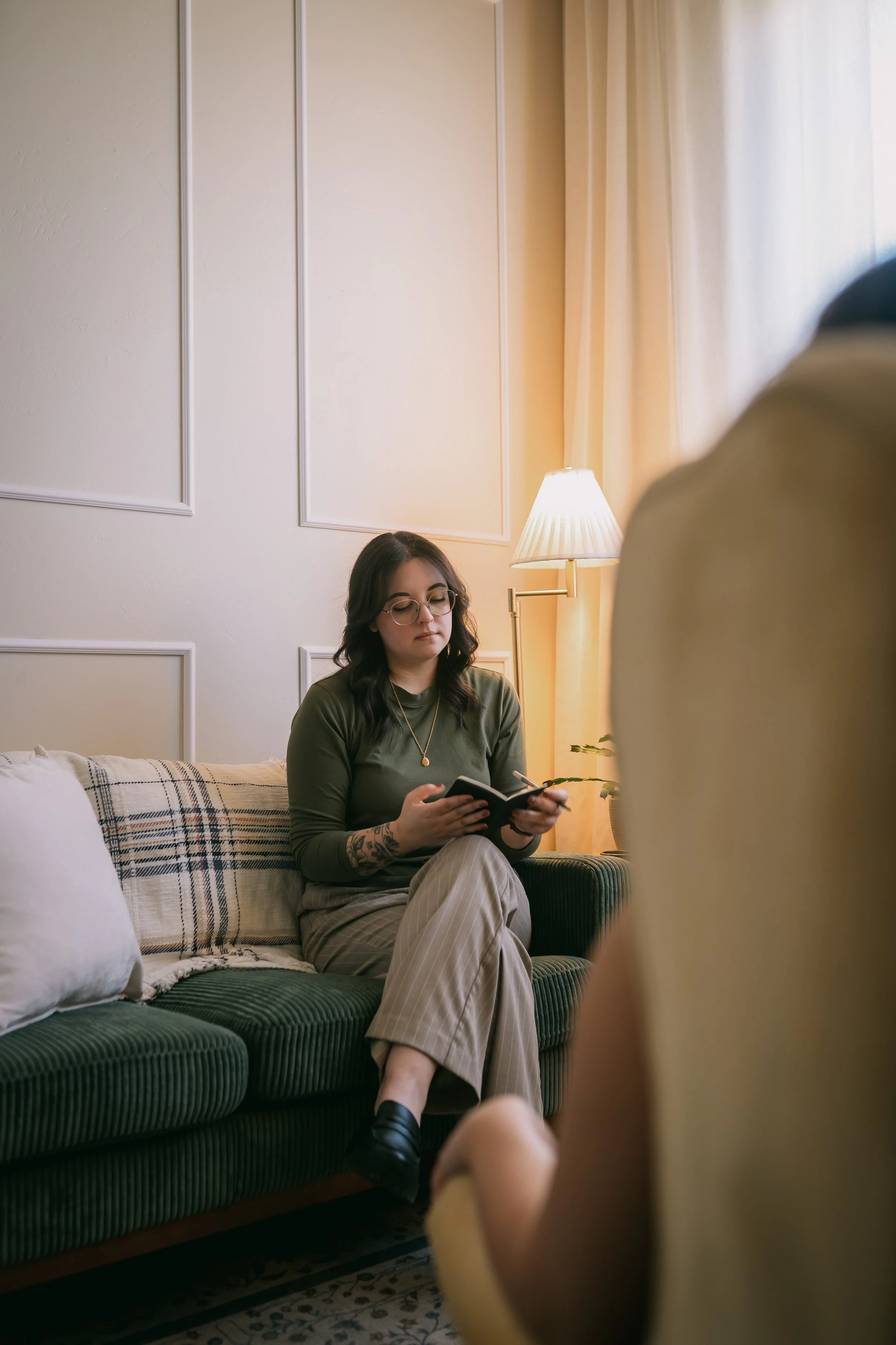 Joanna Jackson, LPC, sitting on a green couch, reviewing her notes in her notebook, while listening to a client.