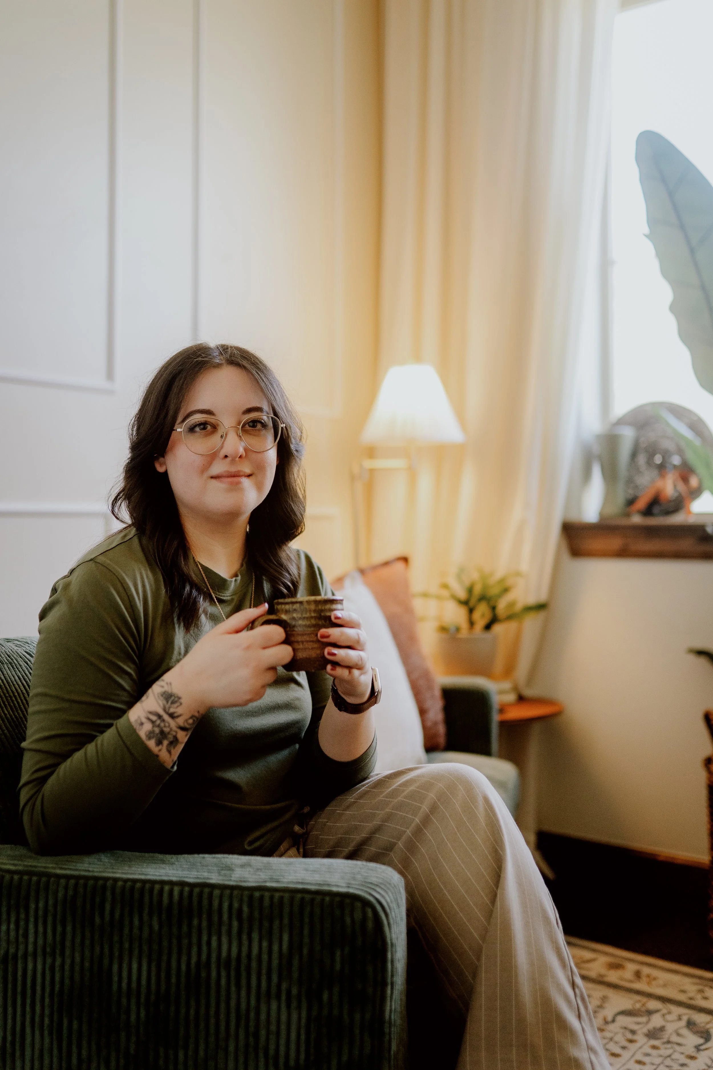Joanna Jackson, LPC, sitting on a green couch in her office, while holding a coffee mug and looking compassionate.