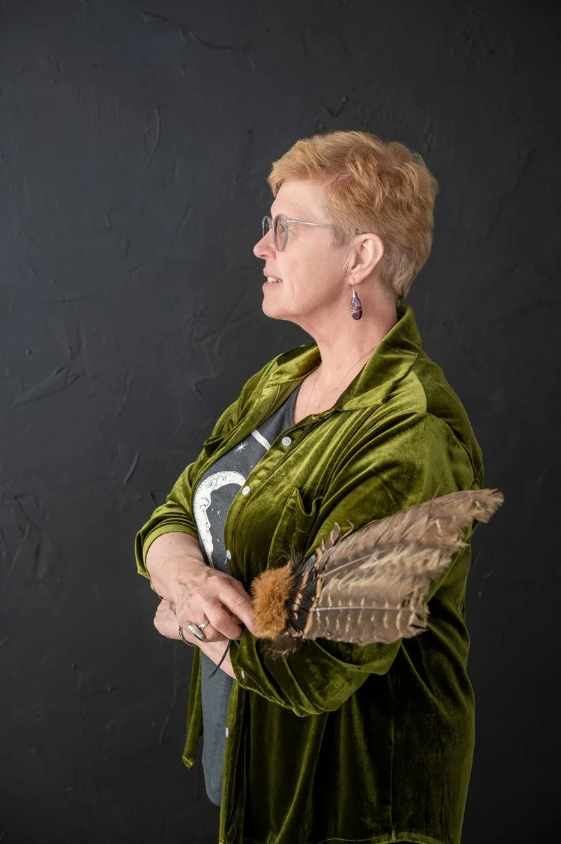 Profile photo of Susan Lynn in a green velvet jacket, looking thoughtfully to the side against a dark background, reflecting intuitive wisdom and grounded spirituality.