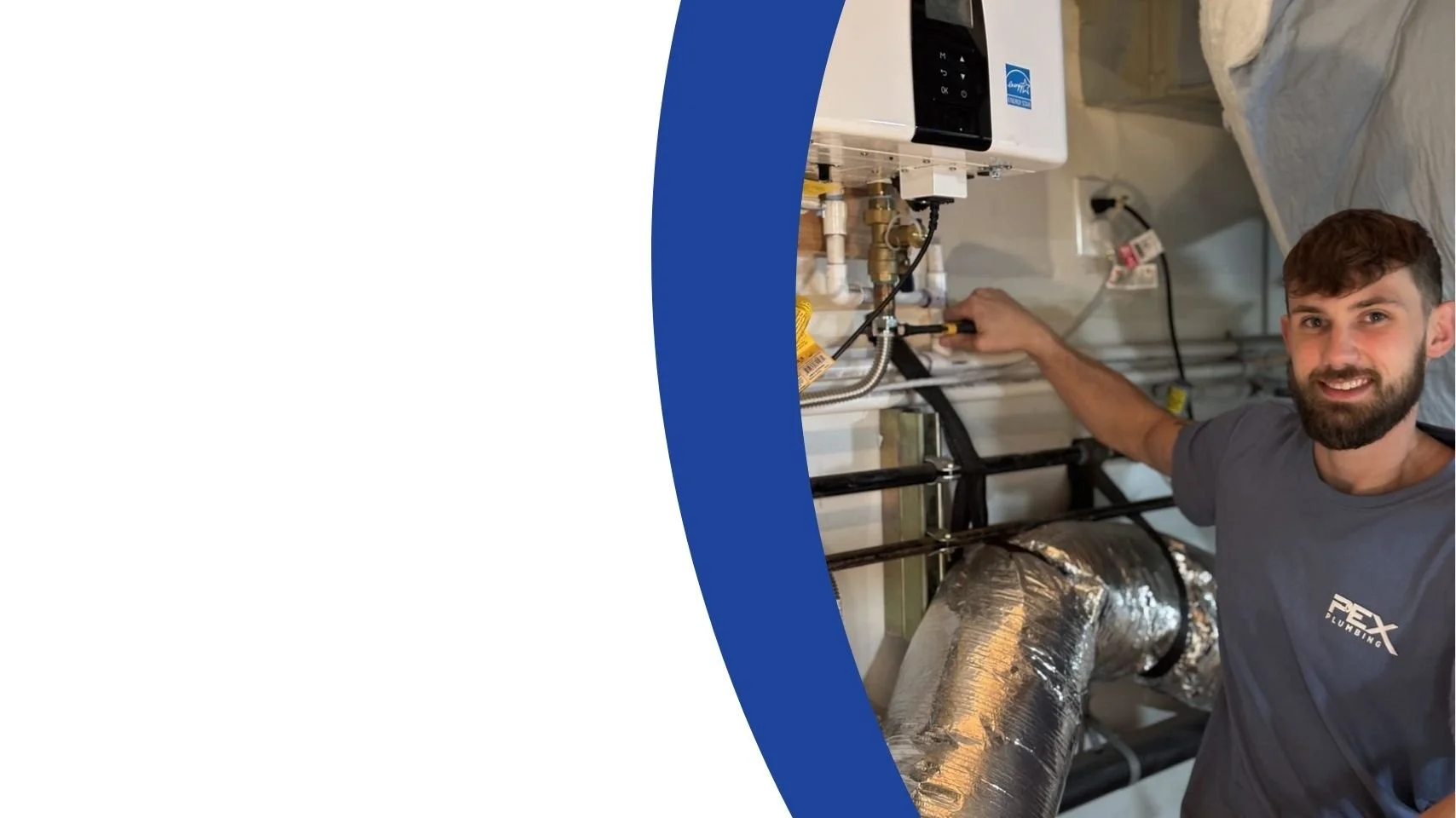 A man with brown hair and a beard, wearing a gray T-shirt with a logo, is working on plumbing or HVAC equipment.