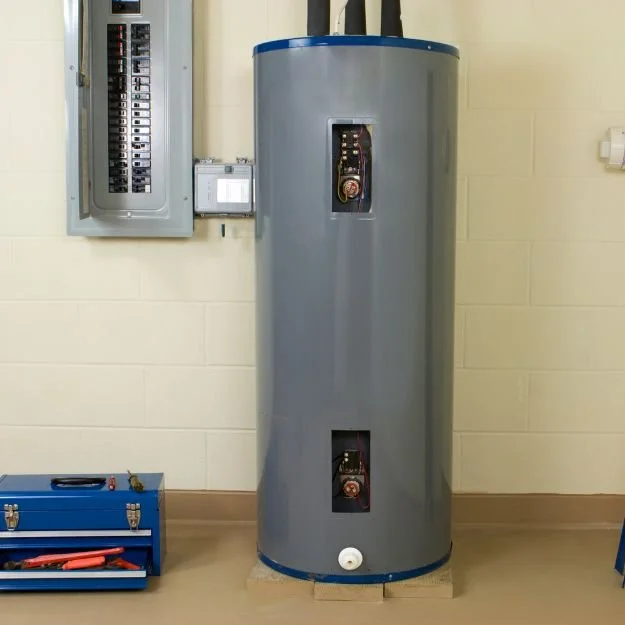A water heater tank in a utility room with access panels, electrical panel, and a toolbox on the floor nearby.