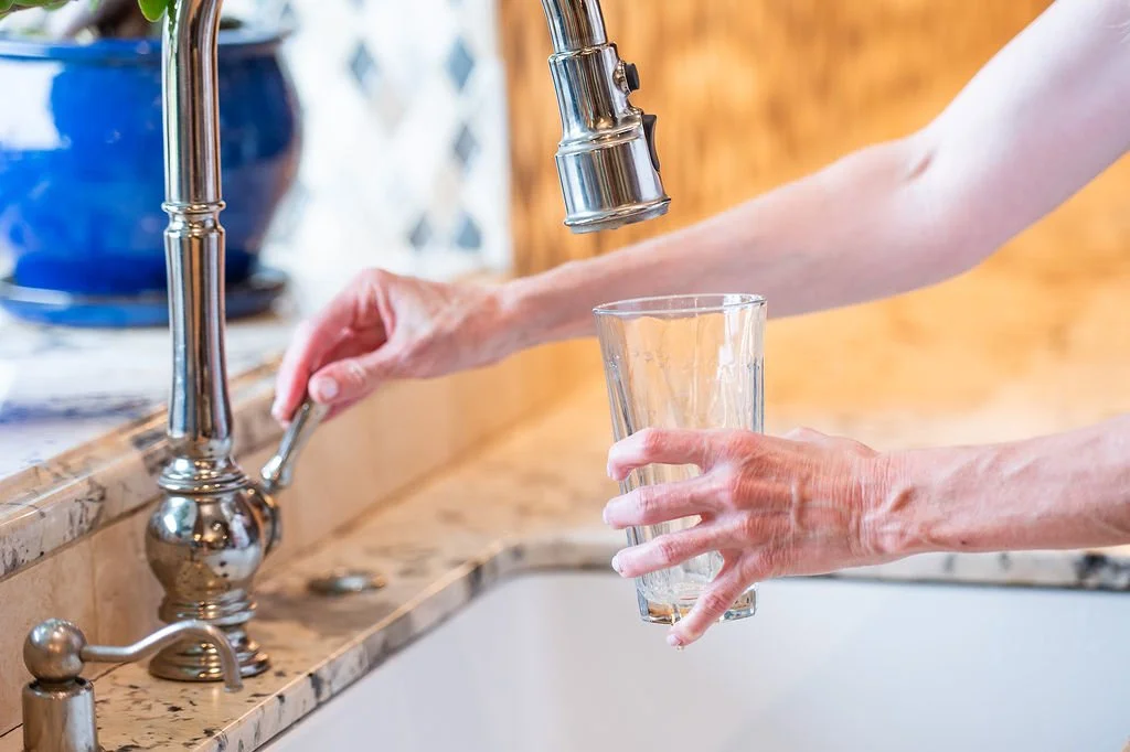 Person filling a glass with water from a kitchen faucet.