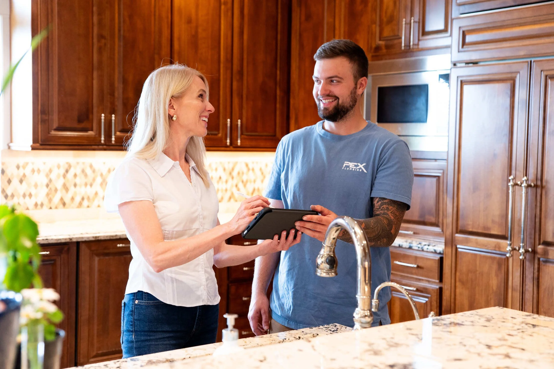 A woman and a man talking and smiling in a kitchen, with the woman holding a tablet or notepad.