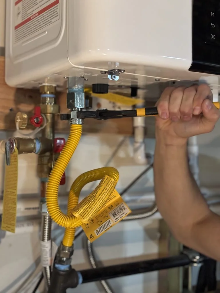 A person repairing or installing a water heater or boiler, working on the plumbing connections with a wrench.