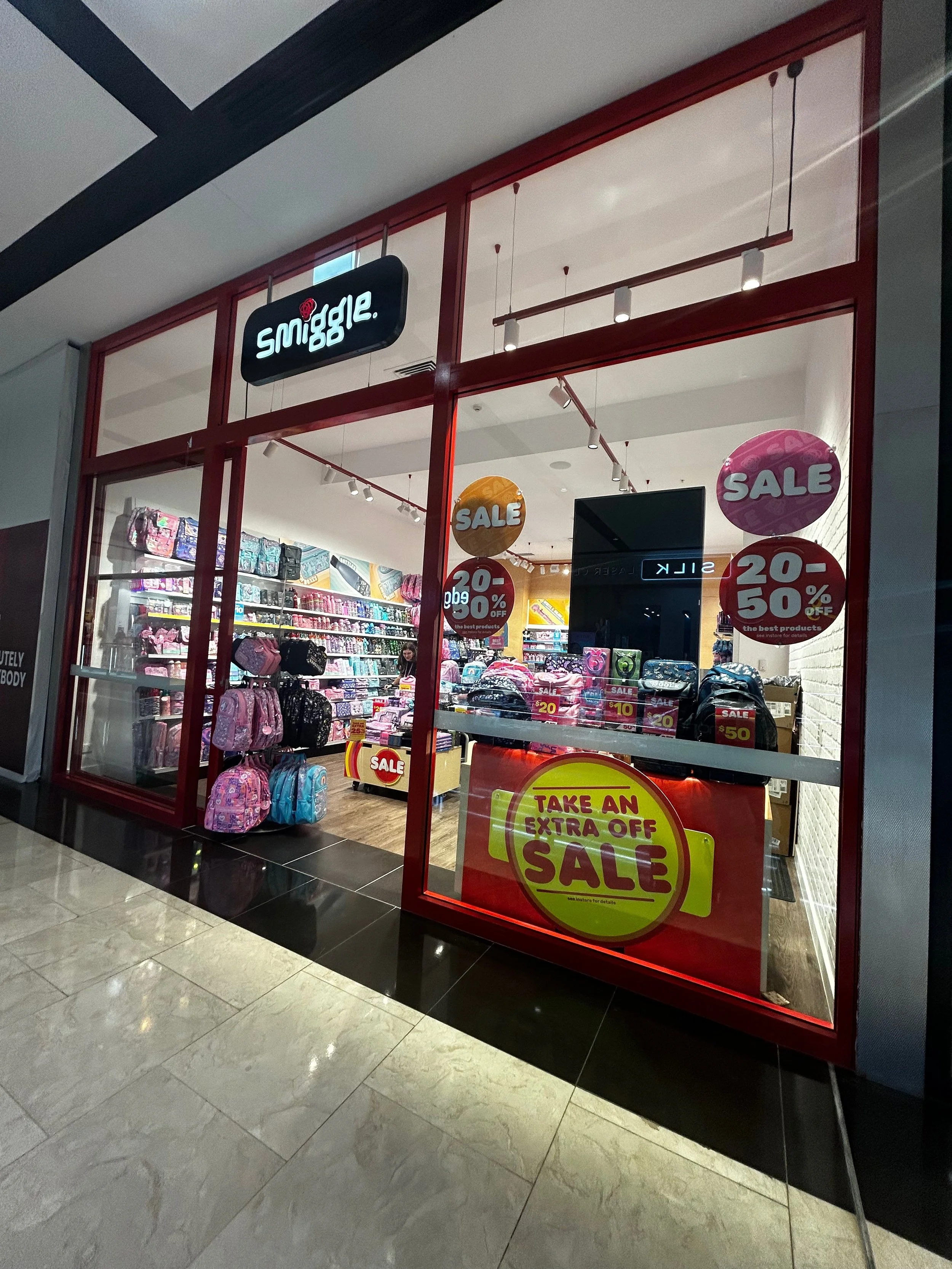 Storefront of a retail shop selling backpacks, with sale signs and discounts displayed in the window.