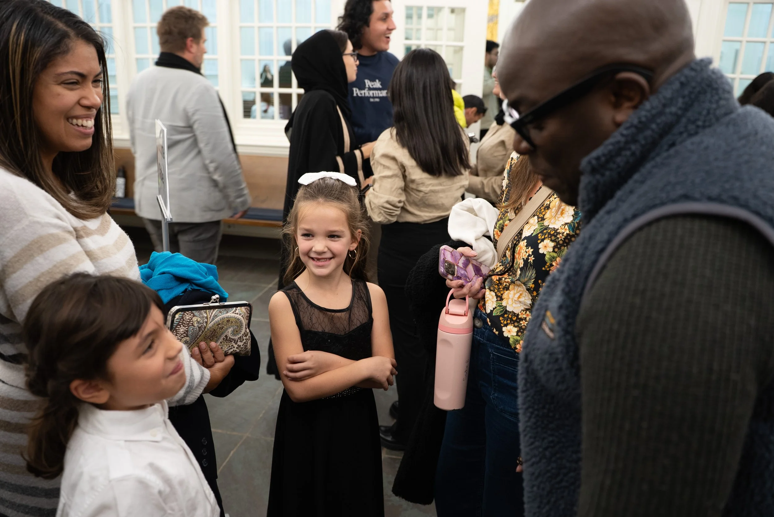 A group of children and adults smiling and chatting at an indoor social gathering.