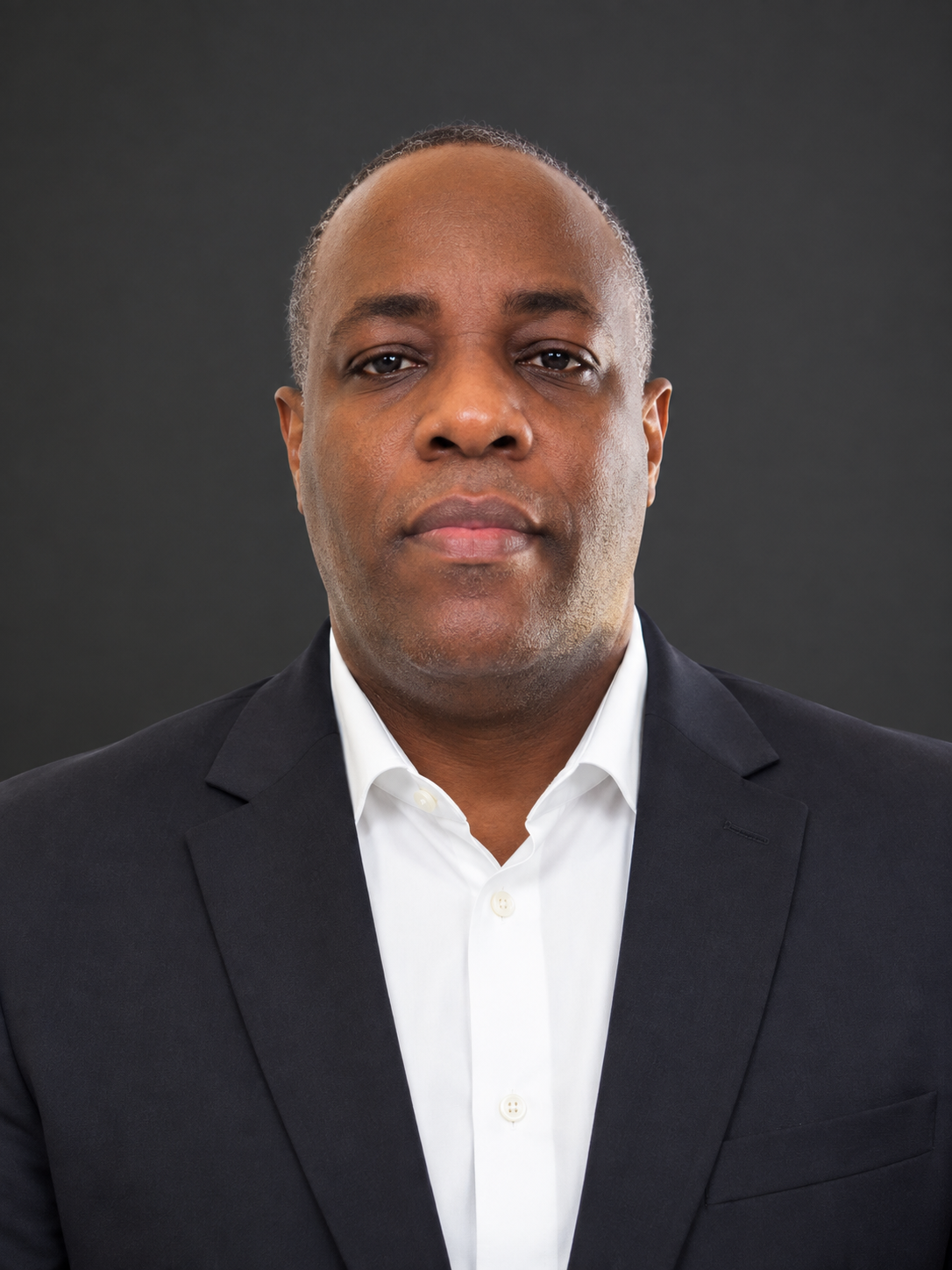 Professional headshot of a man wearing a dark suit and white shirt against a dark background.