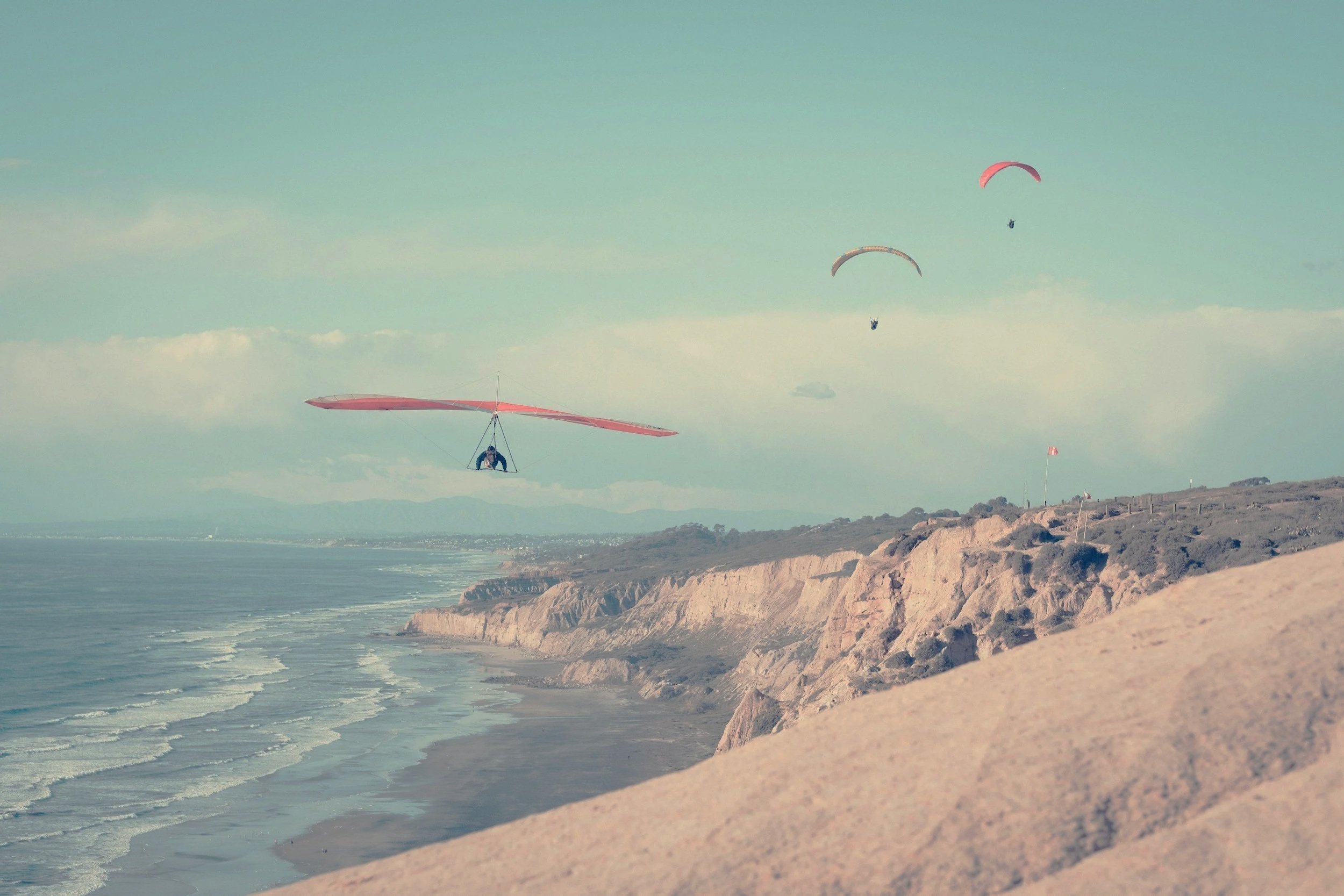 Paragliders flying over a coastal cliff along the ocean.