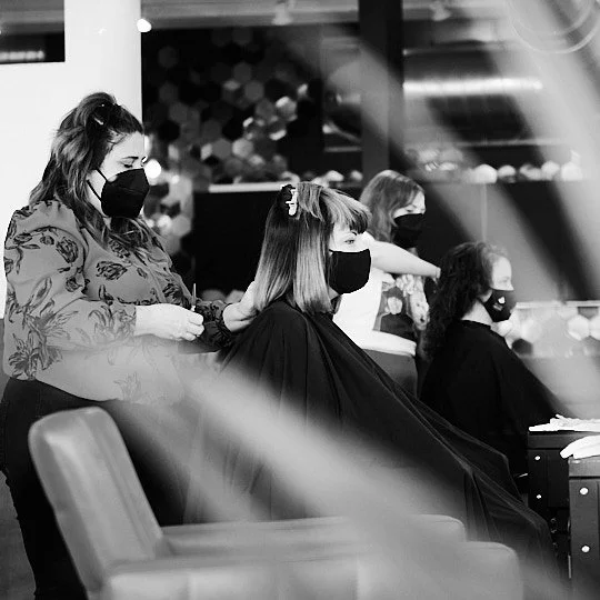 Women wearing masks, one getting a haircut in a salon.