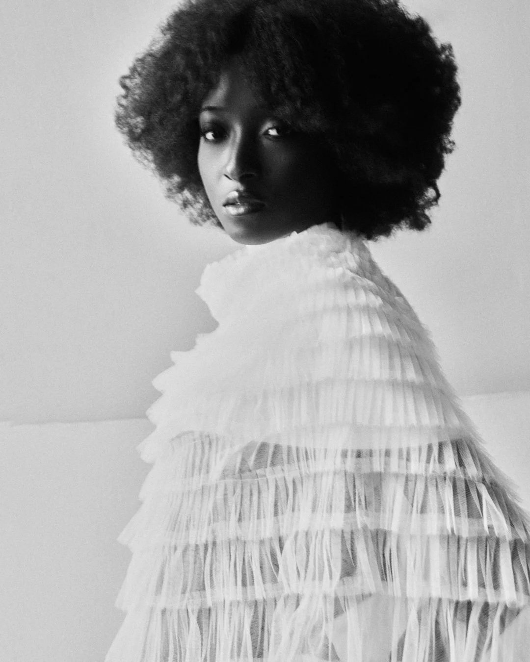Black and white portrait of a woman with natural curly hair wearing a high-neck, ruffled dress.