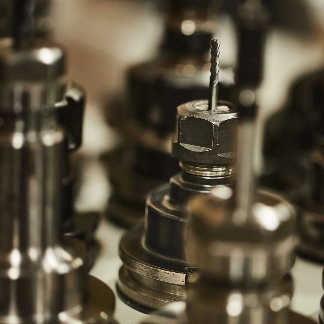 Close-up of metal industrial machine parts, possibly machining tools or components, with a focus on a threaded rod and a nut.
