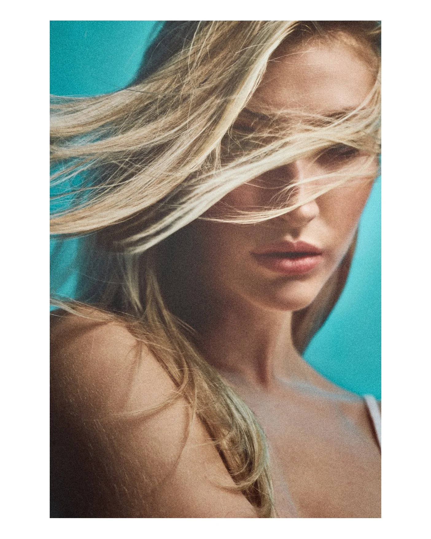 Close-up of a woman with long blonde hair partially covering her face, with a turquoise background.