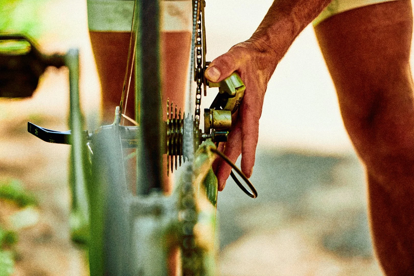 Close-up of a person handling the chain and gears of a bicycle, with a blurred background.