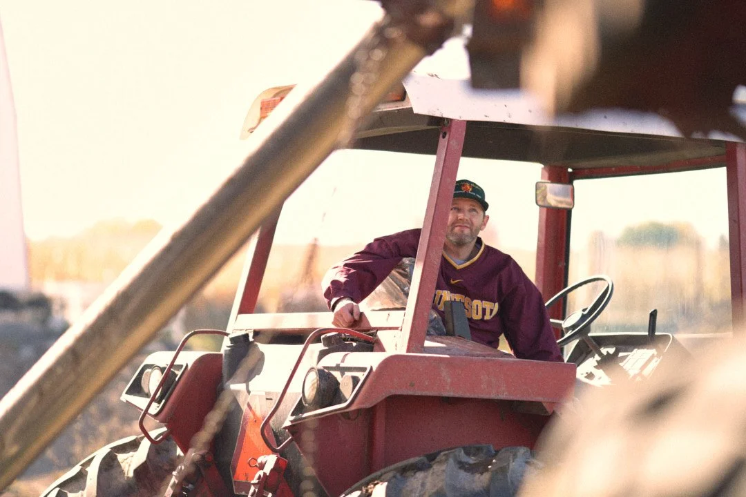 A man wearing a Minnesota Vikings jacket and cap sitting in a red tractor.