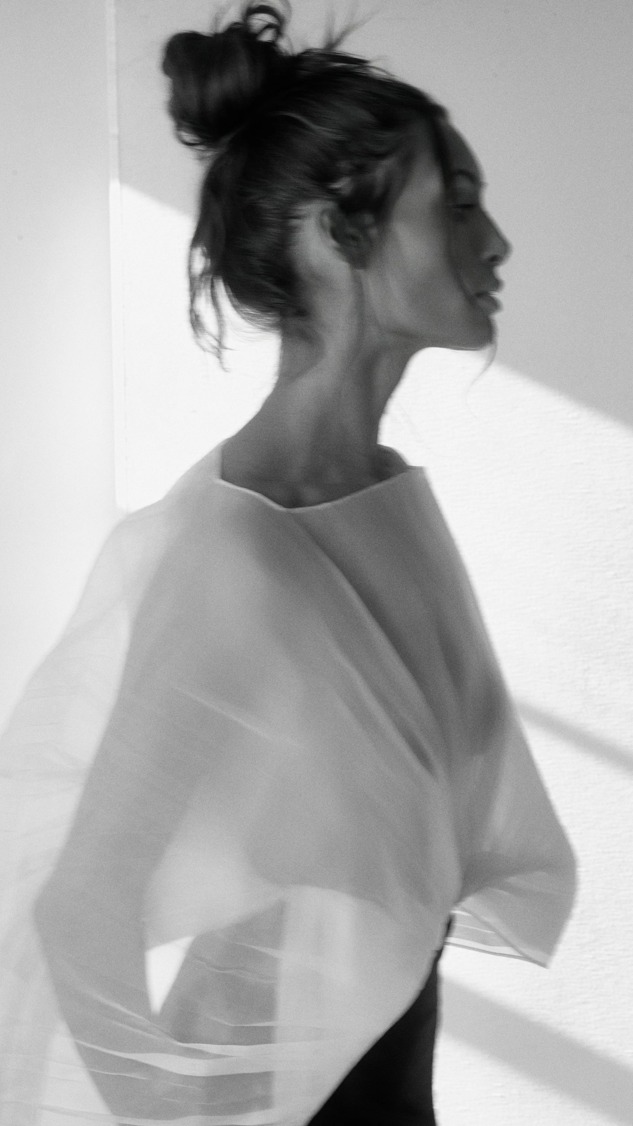 A black and white photo of a woman with her hair in a messy bun, seen in profile, with her eyes closed and a calm expression.