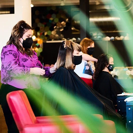 Hair salon with customers getting haircuts, all wearing black face masks.