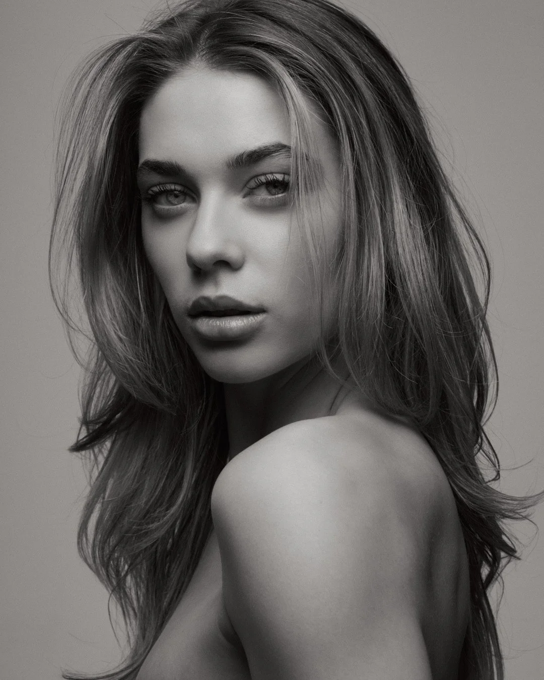 Black and white portrait of a young woman with wavy hair, looking at the camera with a slightly open mouth.