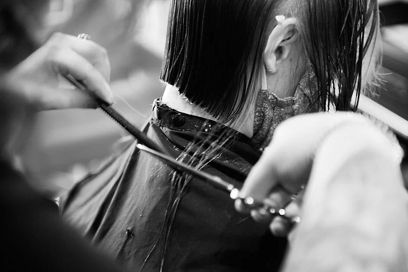 A person getting a haircut at a salon, with the focus on the hairdresser cutting the client's hair.