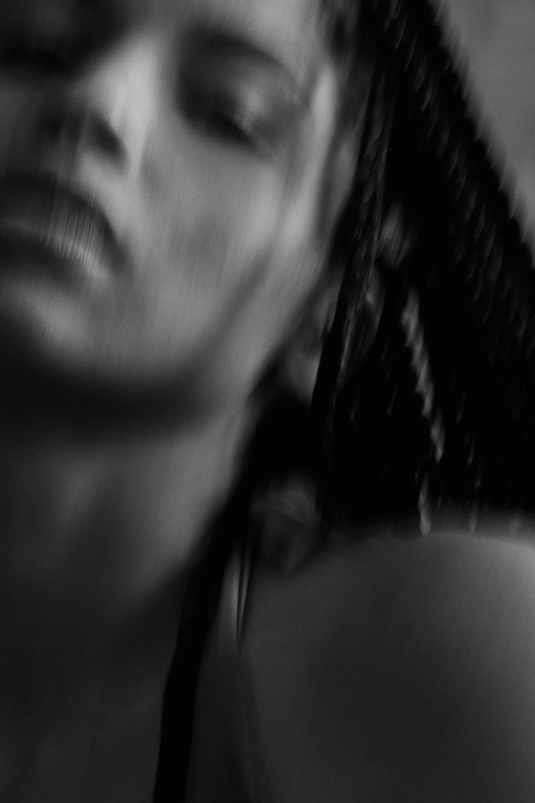 A close-up black and white photo of a woman's face, showing her lips, nose, and one eye, with textured hair on the side.