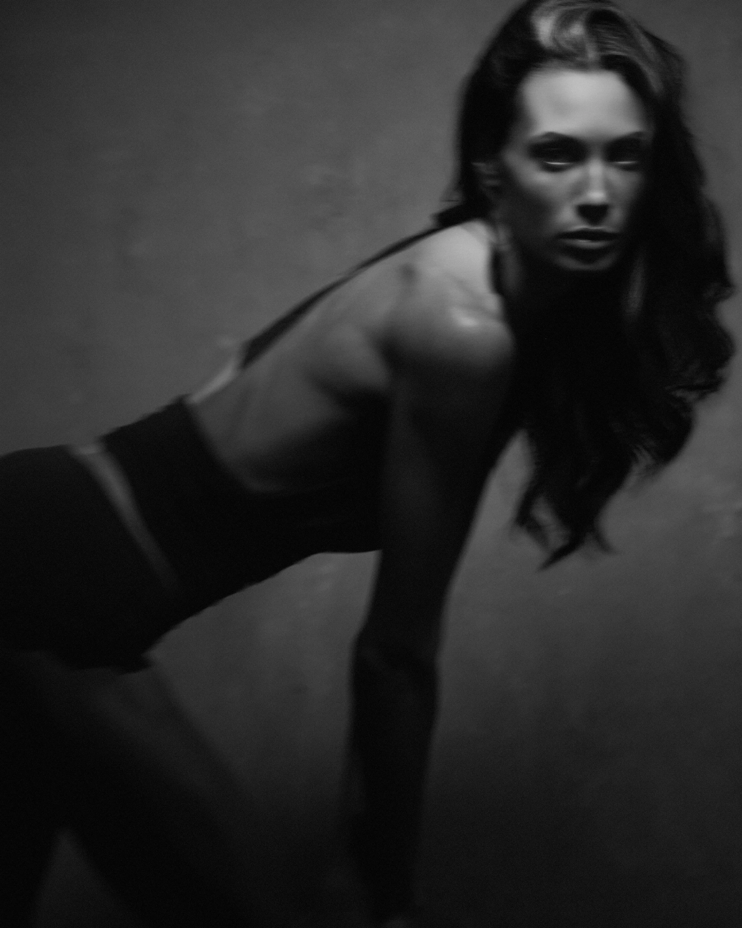 Black and white photo of a woman with long hair in a crouching pose, looking at the camera.