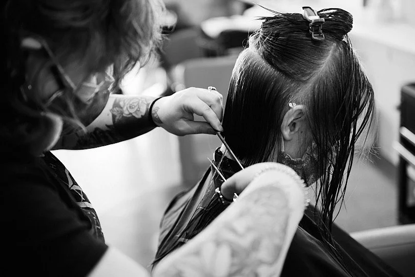 A hairstylist cutting a woman's hair in a salon, with the woman seated and her hair wet.