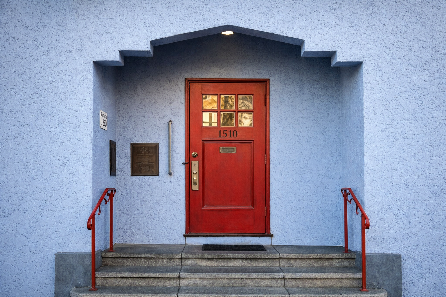Red front door with the number 1510, surrounded by blue textured wall, with stairs and red handrails leading up to it.