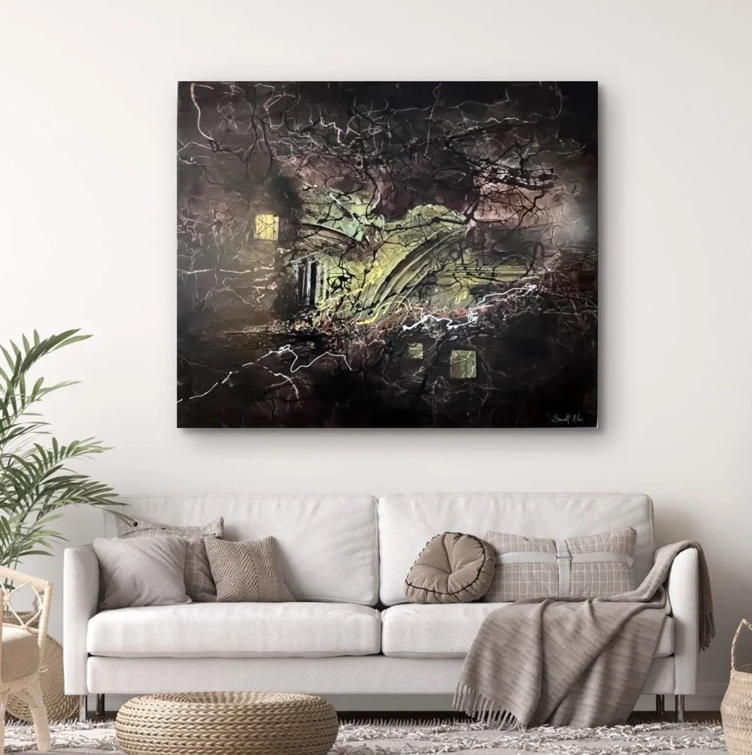 A modern living room with a white sofa, beige and gray pillows, a light brown blanket, and a large abstract painting with dark colors and light streaks hanging on the wall.