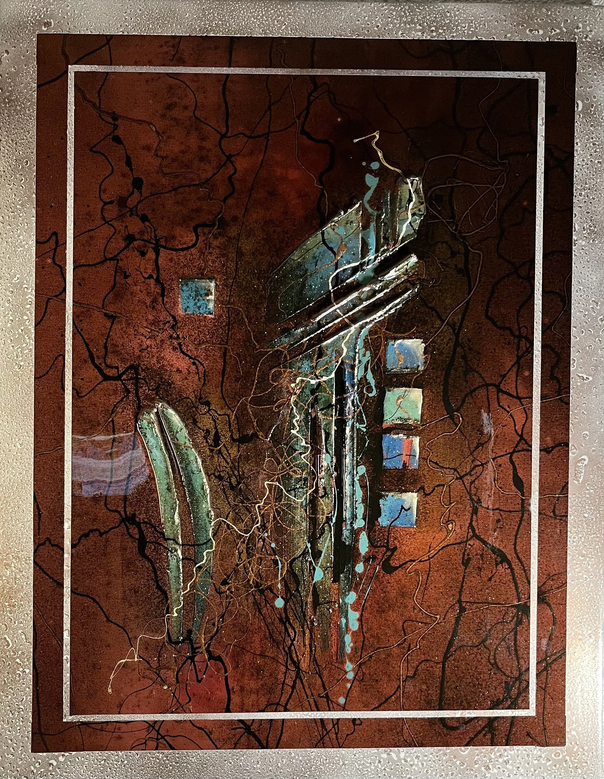 Abstract artwork with a brown background, black lines resembling tree branches, and a central vertical strip of blue and green paint with white accents. The image is bordered by a silver dotted frame.