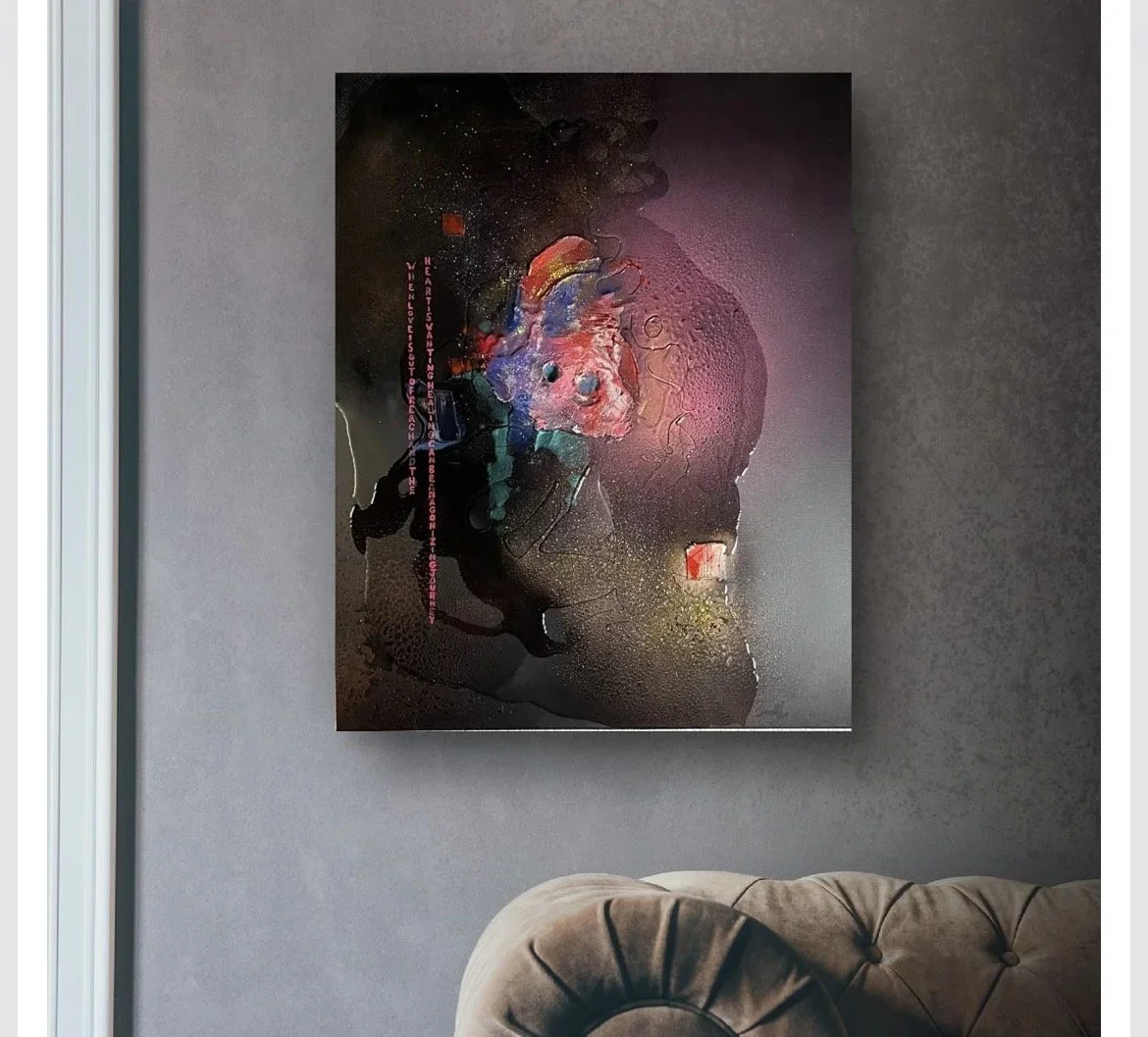 Abstract modern art painting with dark background, splashes of vibrant colors, and textured surface, hanging on a gray wall above a beige tufted armchair.