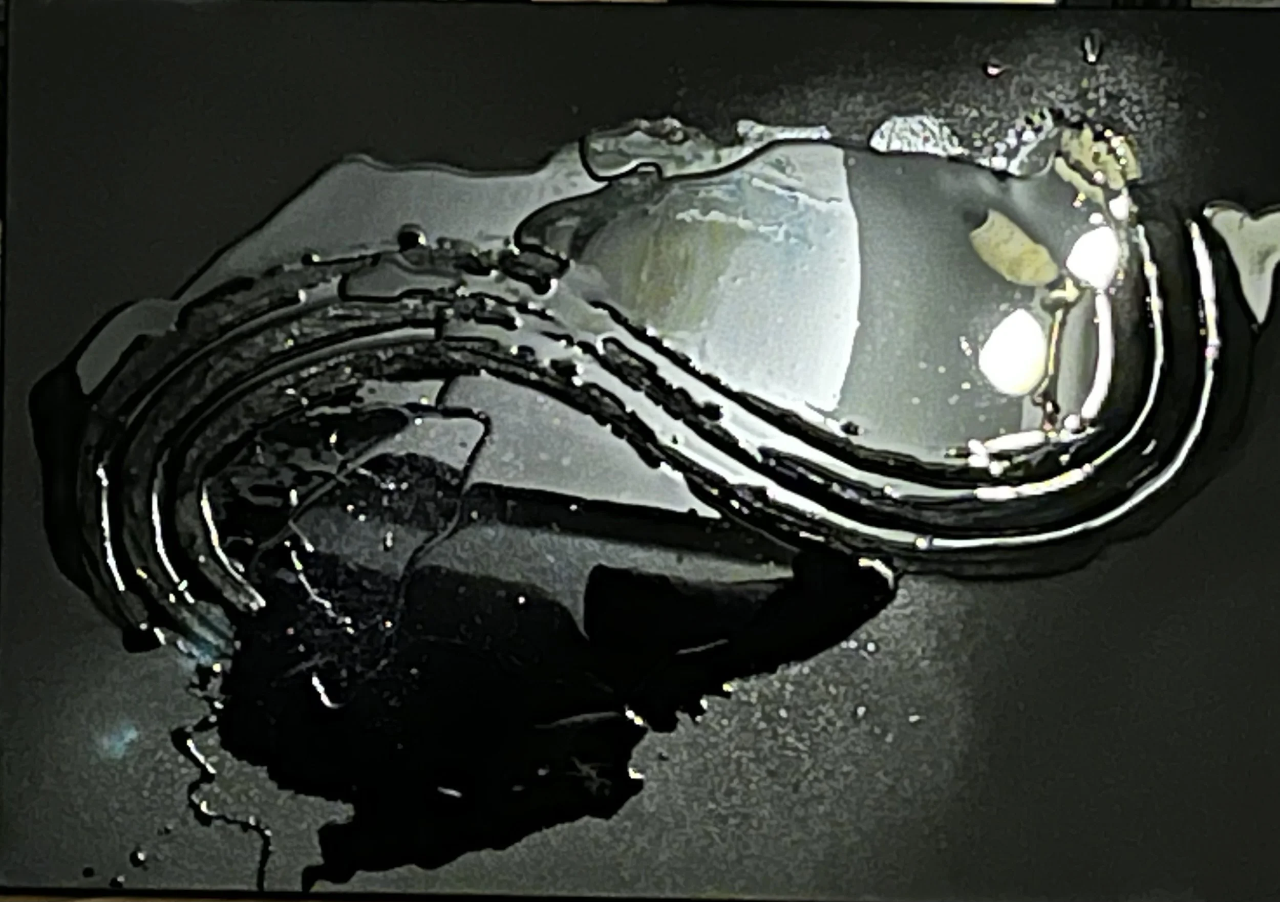 Close-up of a watch with a dark band on a dark surface with some liquid spilled around it.