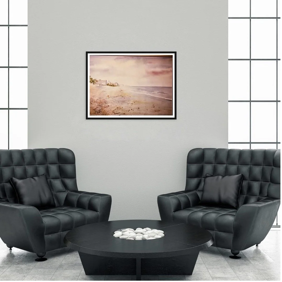Modern lounge with two black leather armchairs, a black coffee table with white stones, a framed beach photo on the wall, and large windows in the background.