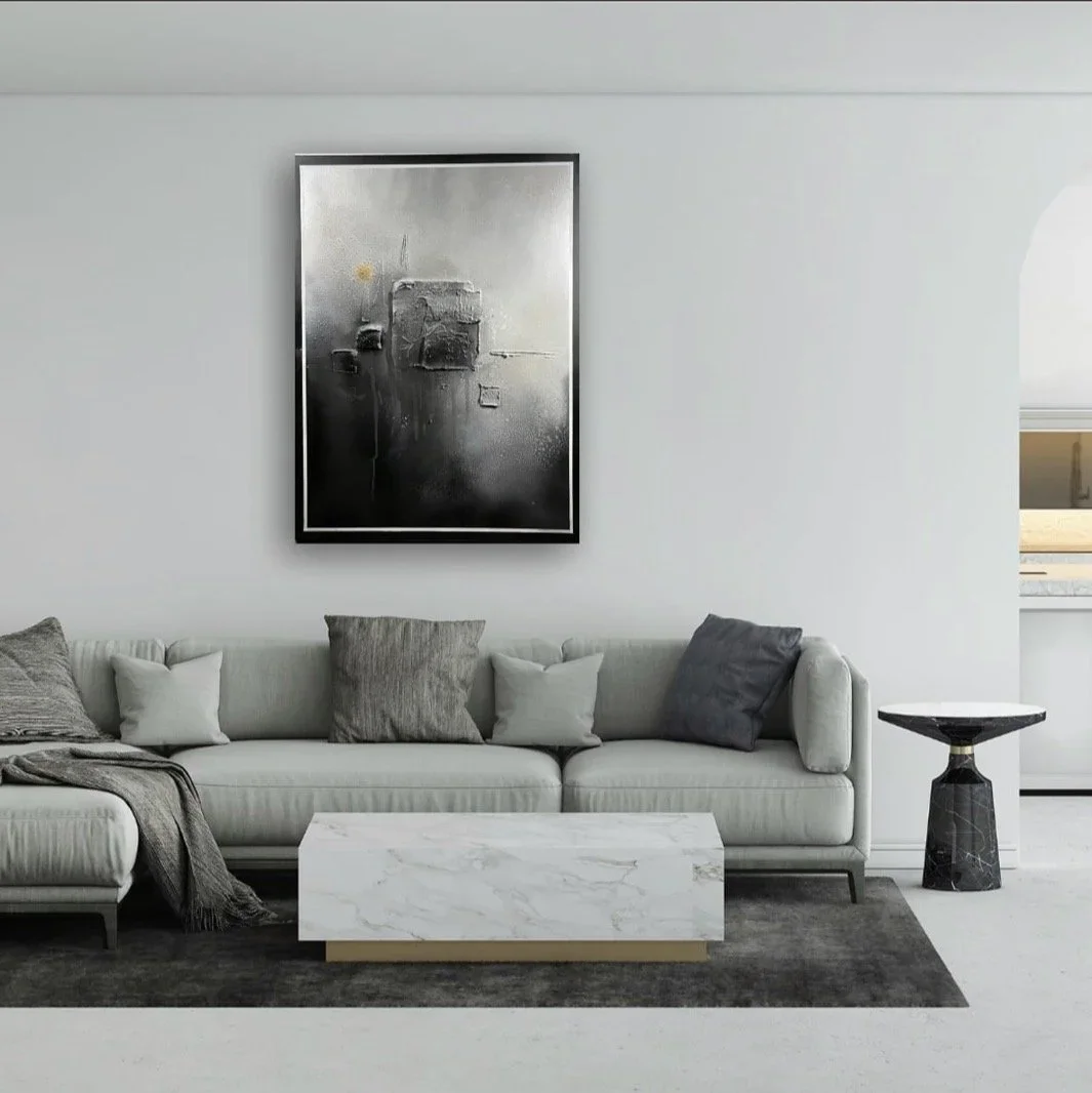 Modern minimalist living room with a white sofa, gray throw blanket, gray and white cushions, abstract black and white artwork on the wall, a white marble coffee table, black side table, and a gray area rug.