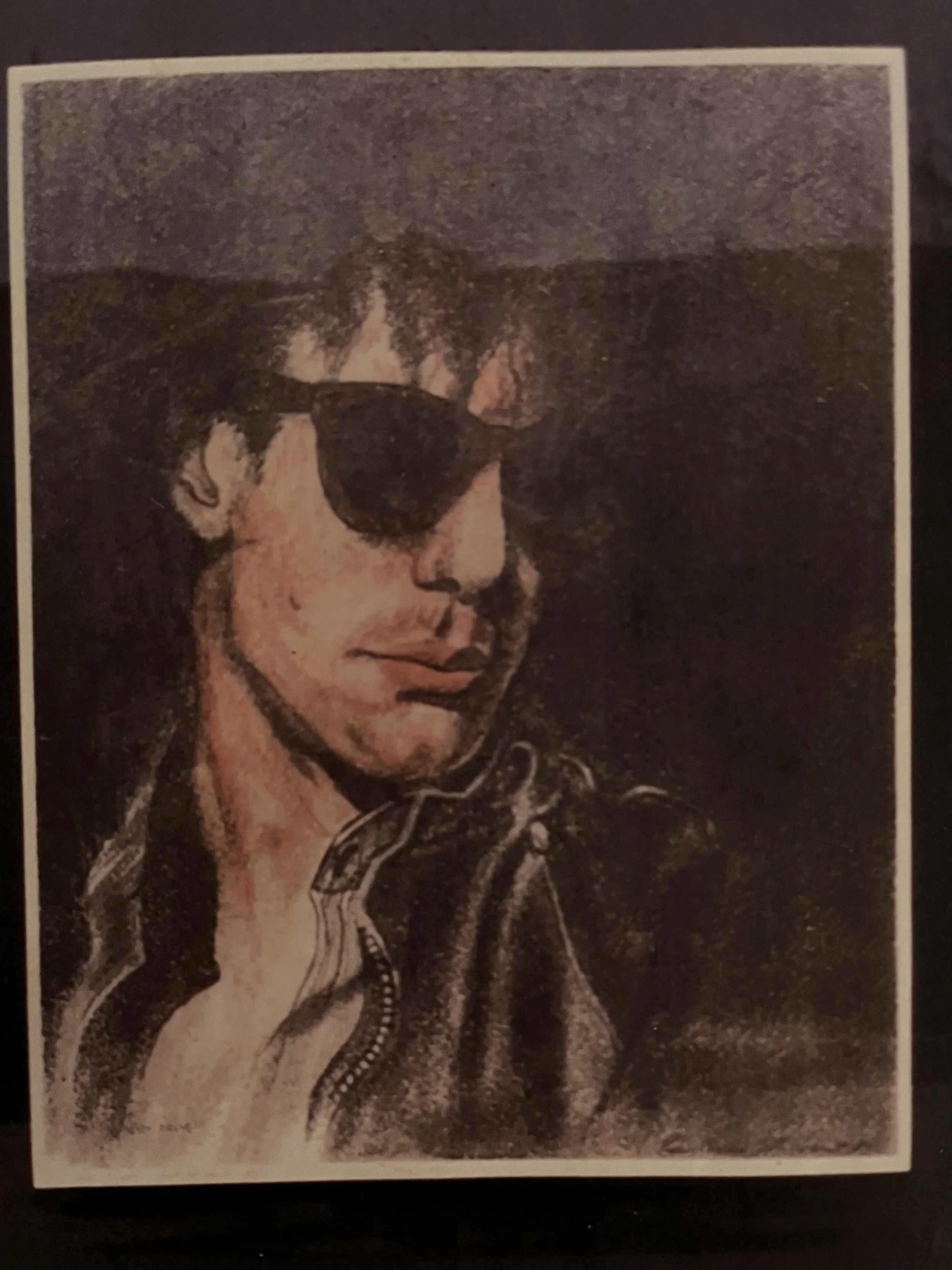 A close-up painting or photograph of a woman with short dark hair, wearing sunglasses with dark lenses, a leather jacket with a collar, and a striped shirt underneath.